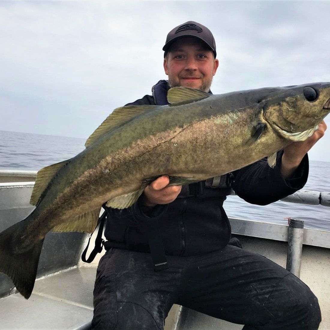 Mann i mørke klær og caps holder stor fisk